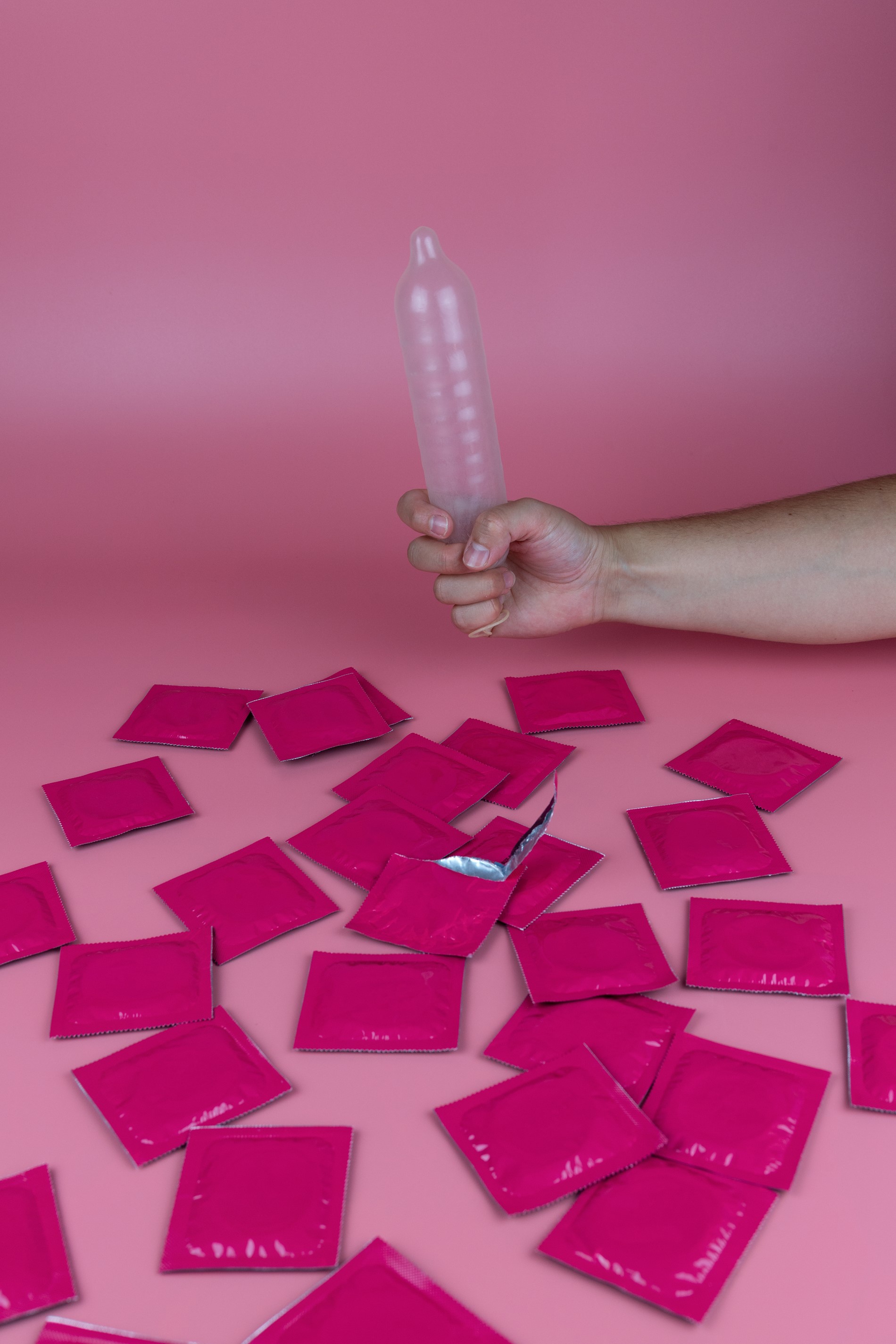 Person holding an inflated condom, surrounded by packets of condoms